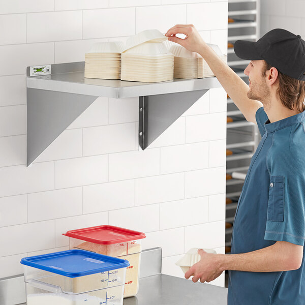 A man in a blue shirt and black cap standing in a kitchen looking at a Regency stainless steel wall shelf.