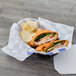 A blue check deli sandwich wrap with a sandwich and chips in a basket.