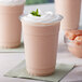 A plastic cup of pink liquid with whipped cream and mint leaves with a straw in the background.