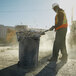 A man in a safety vest throwing debris into a Rubbermaid BRUTE 44 gallon outdoor trash can.