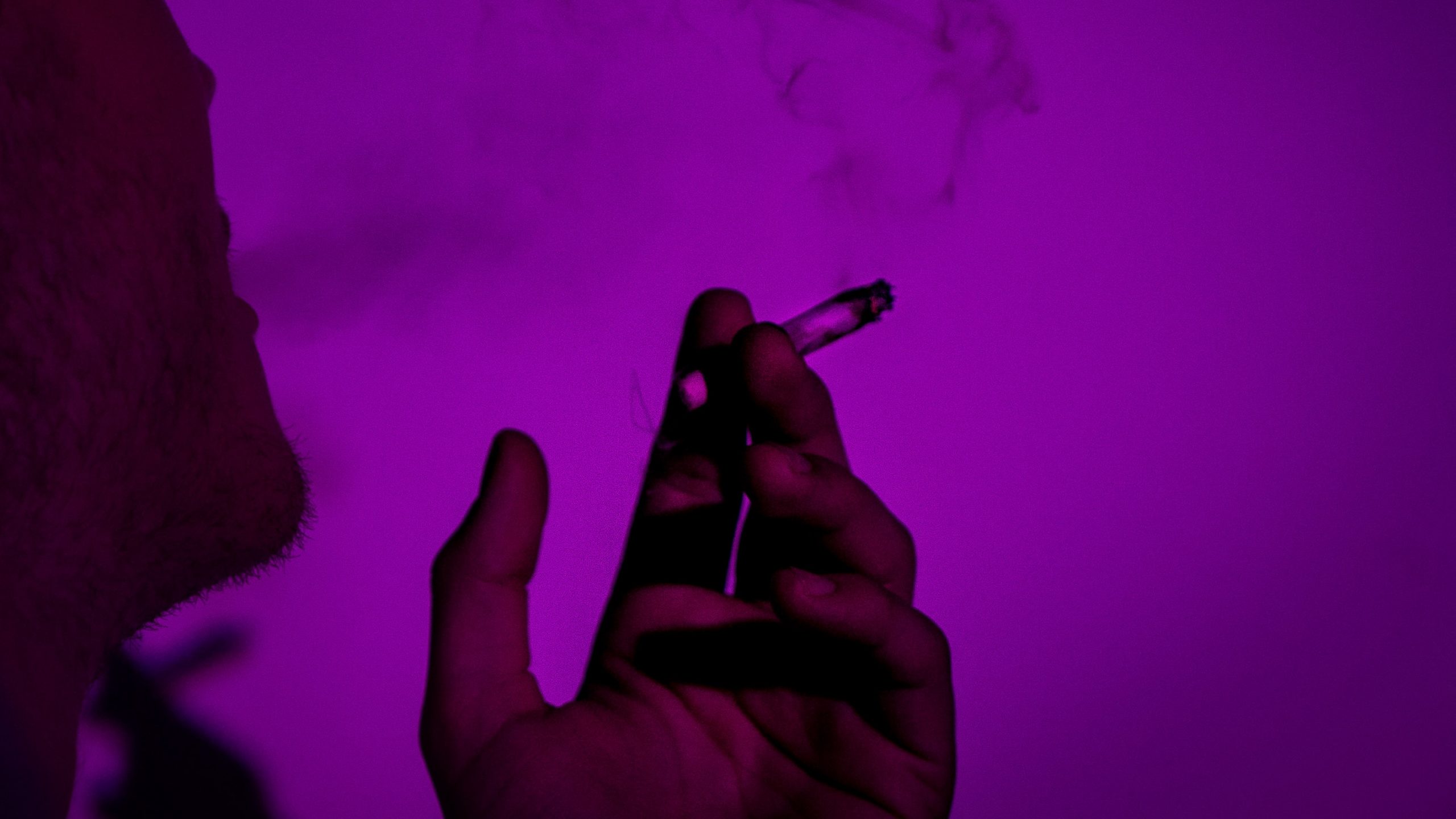 person smoking from a paper joint in a purple background