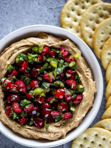 diced jalapenos and cranberries with cilantro over a cream colored dip with crackers on the side