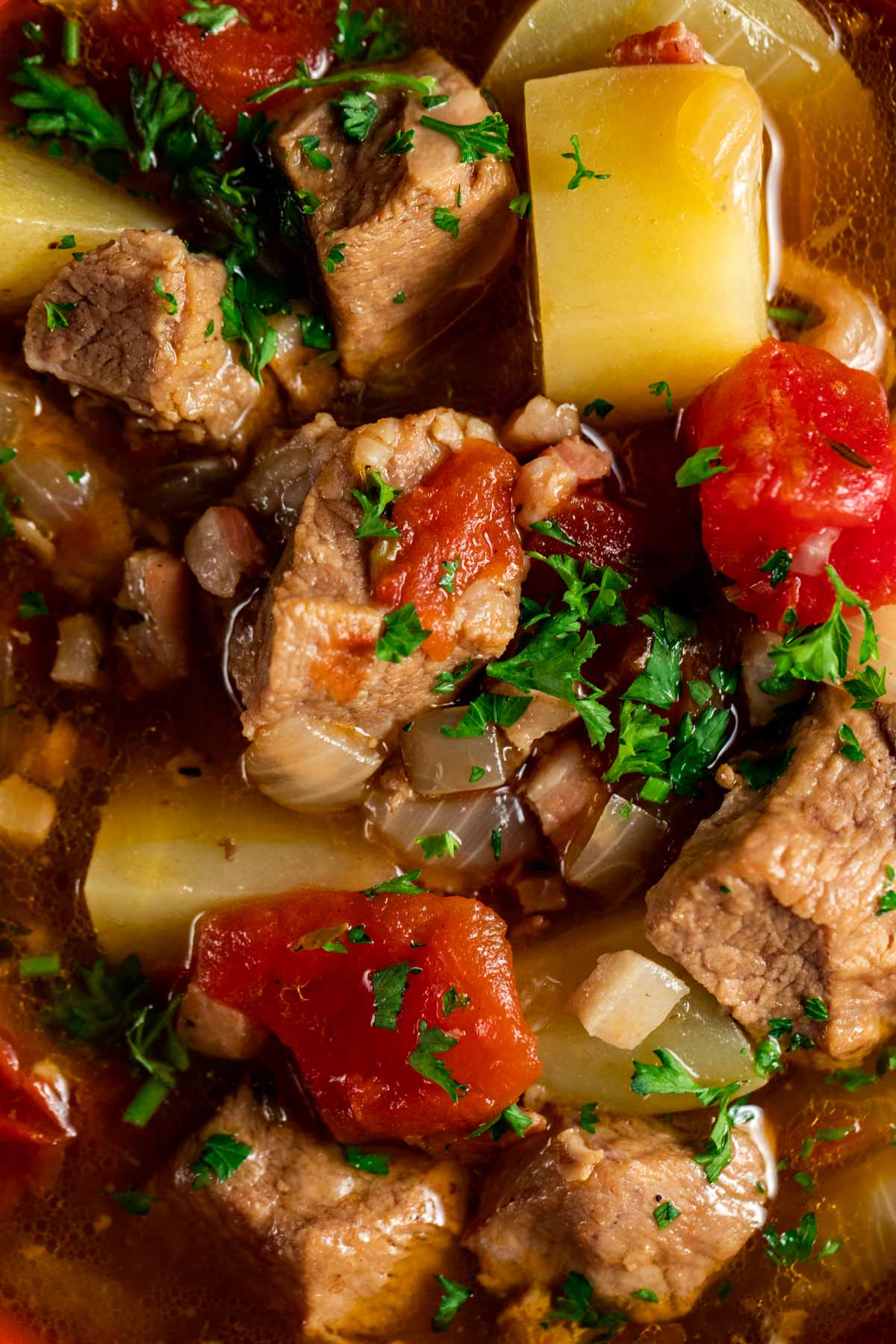 Close up view of stewed veal with potatoes and chopped herbs on top.