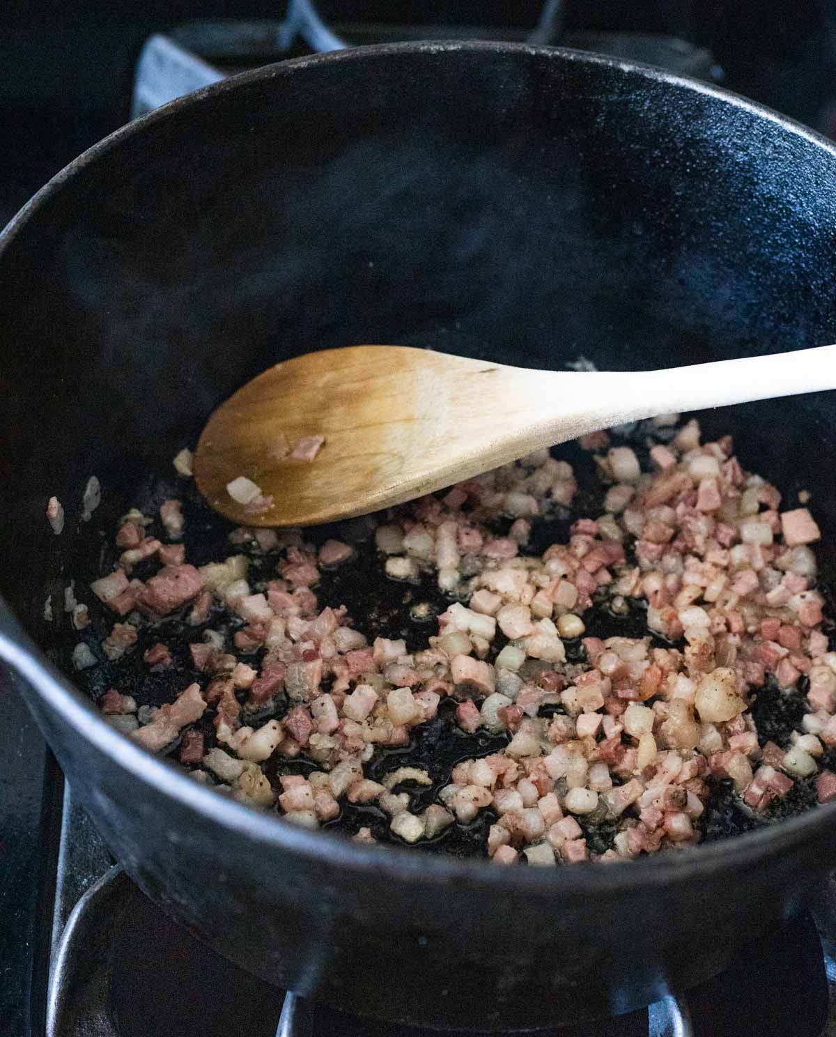 Pancetta browning in a Dutch oven on the stovetop.