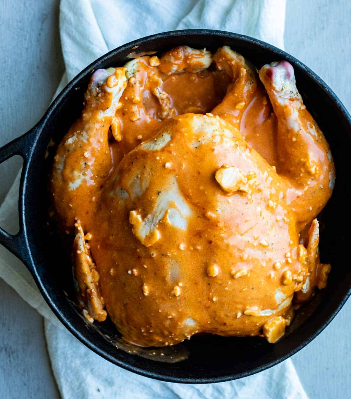 view of a chicken in a bowl with sauce being poured over top prior to cooking