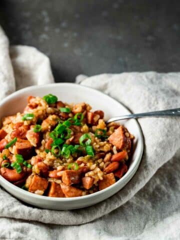 view of red beans and rice in a white bowl with a silver spoon on a white napkin