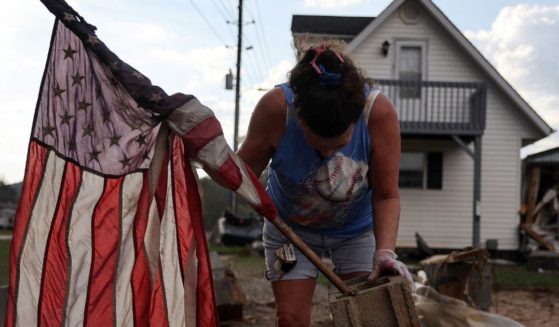 Roxanne Brooks mounts an American flag to a stack of cinderblocks outside her friend's destroyed mobile home (R) in the aftermath of Hurricane Helene flooding on October 6, 2024 in Swannanoa, North Carolina.