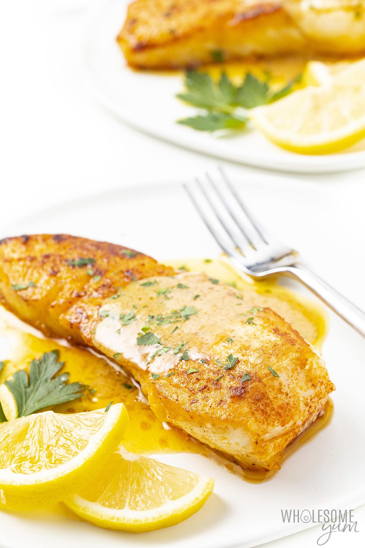 Plated halibut with lemon butter sauce drizzled over it, a sprinkle of fresh parsley, and a fork.