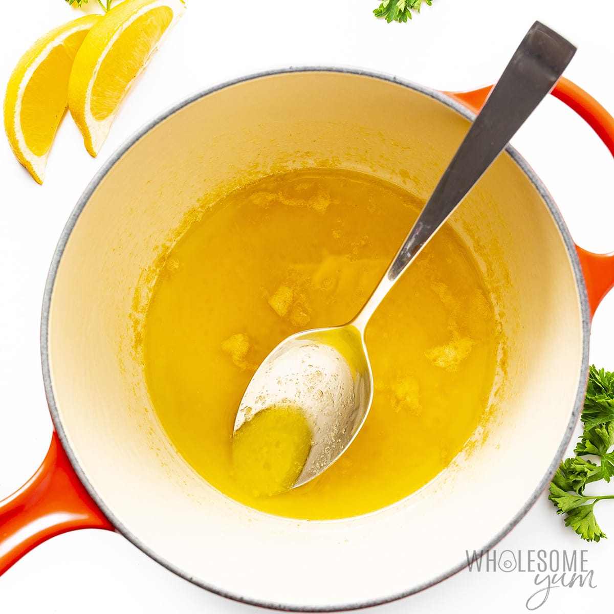 Lemon butter sauce in a saucepan next to lemon wedges and parsley.