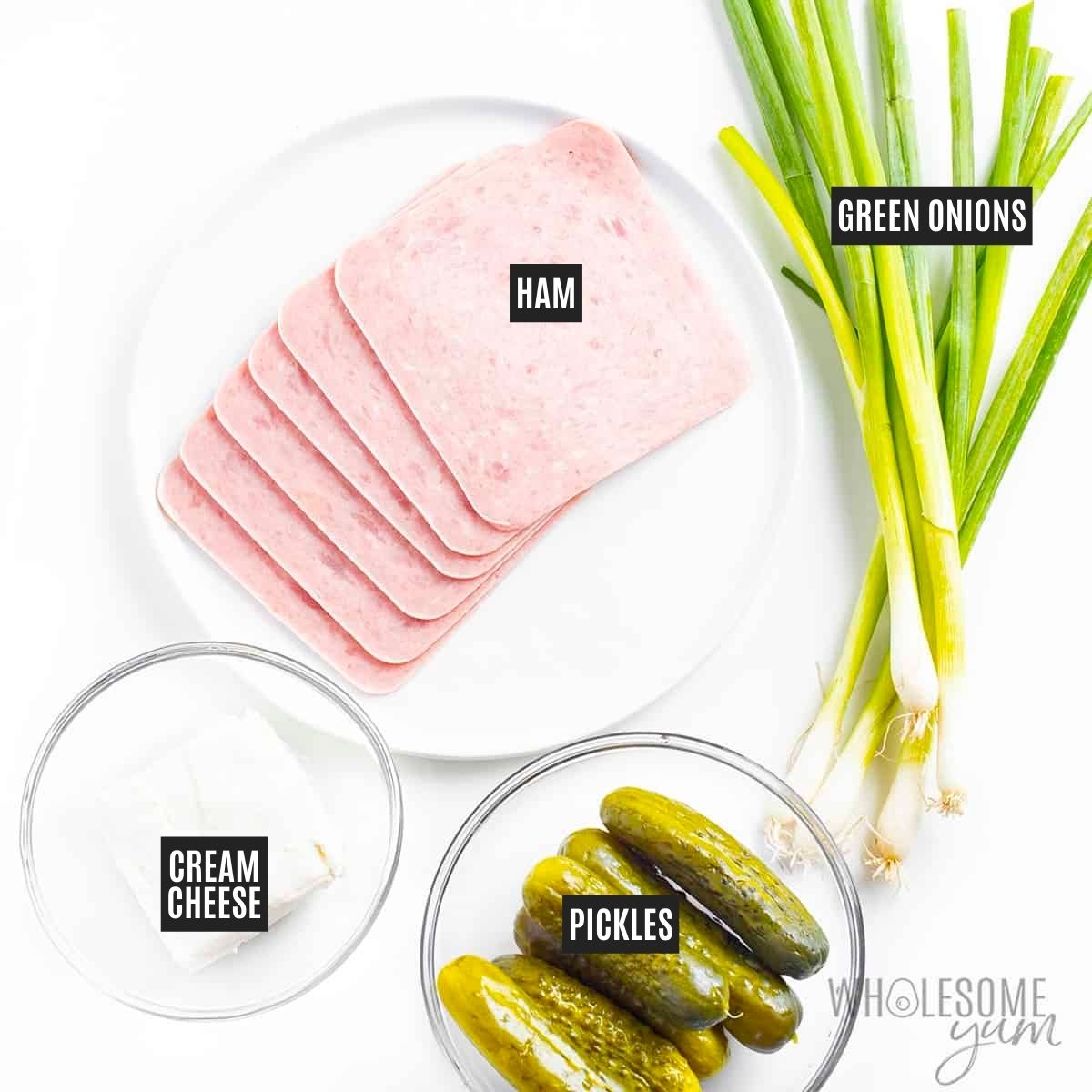 Slices of ham on a plate next to green onions, cream cheese, and pickles.