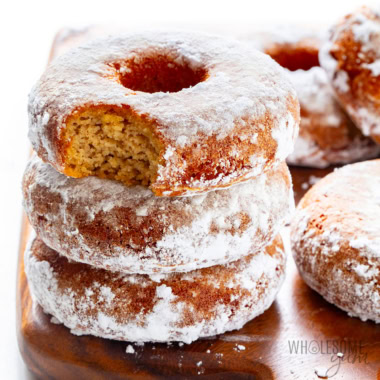 Keto donuts stacked on a cutting board, with a tempting bite taken from the top donut.