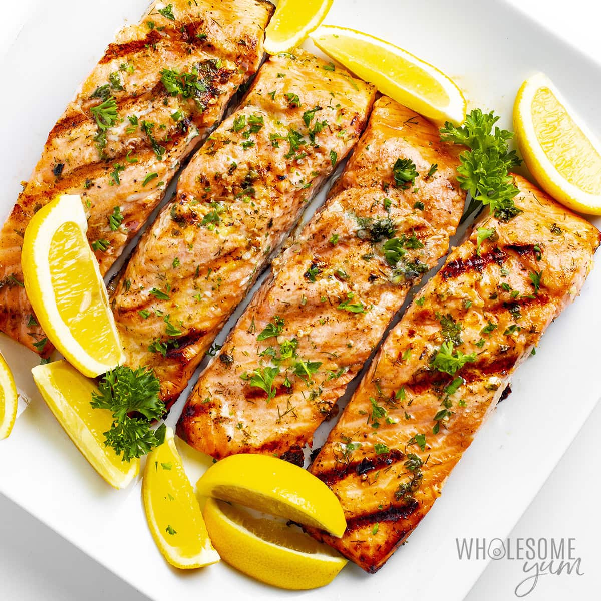 Finished grilled salmon recipe on a plate, garnished with fresh parsley and lemon wedges.