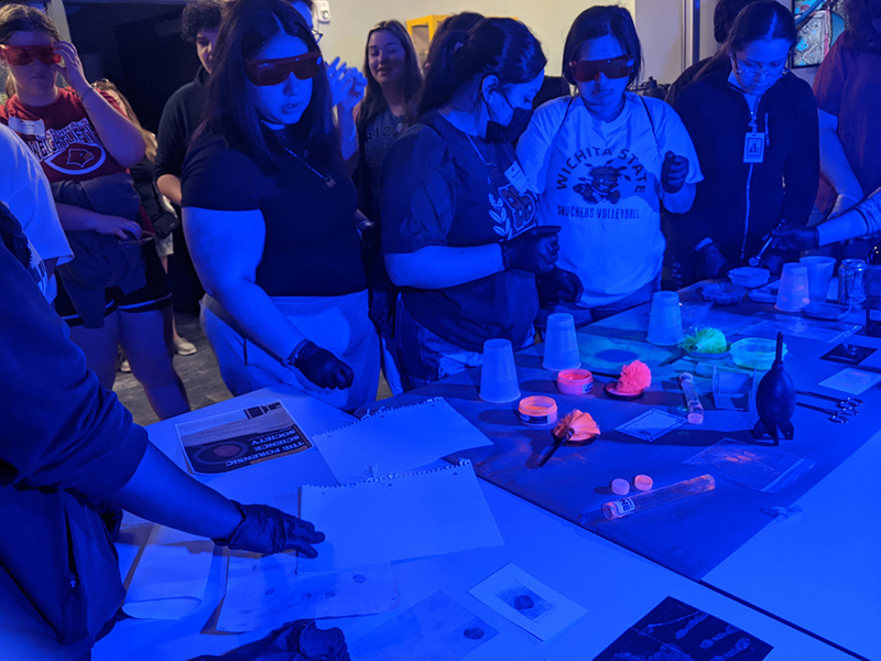 Forensic Science Society members host a mock crime scene demonstration using ultraviolet light to identify materials.