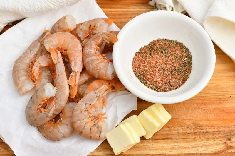 raw shellfish on paper towel, pats of butter and bowl of ground spices all on a wood cutting board