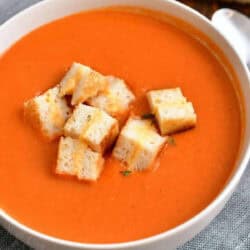 bowl of tomato soup with grilled cheese croutons - grilled cheese sandwich in background.