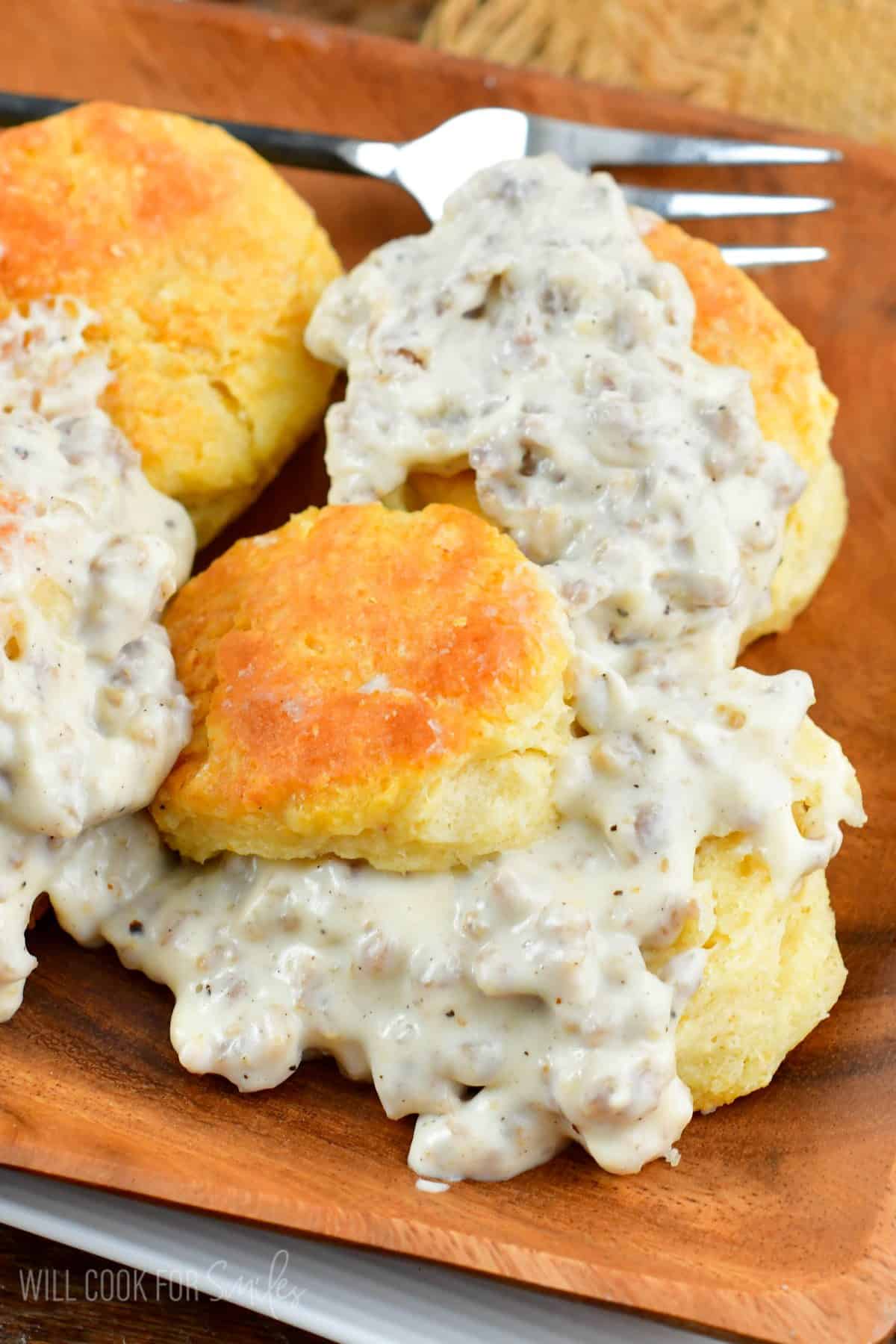 plate with several biscuits with sausage gravy over them on a wood plate.