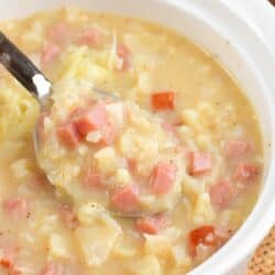 spooning cauliflower ham soup from a white bowl.