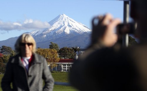 FILE - A man takes a picture of his wife with Mount Taranaki, also known as Mount Egmont, in the background in New Plymouth, New Zealand, Sept. 26, 2011. (AP Photo/Dita Alangkara, File)