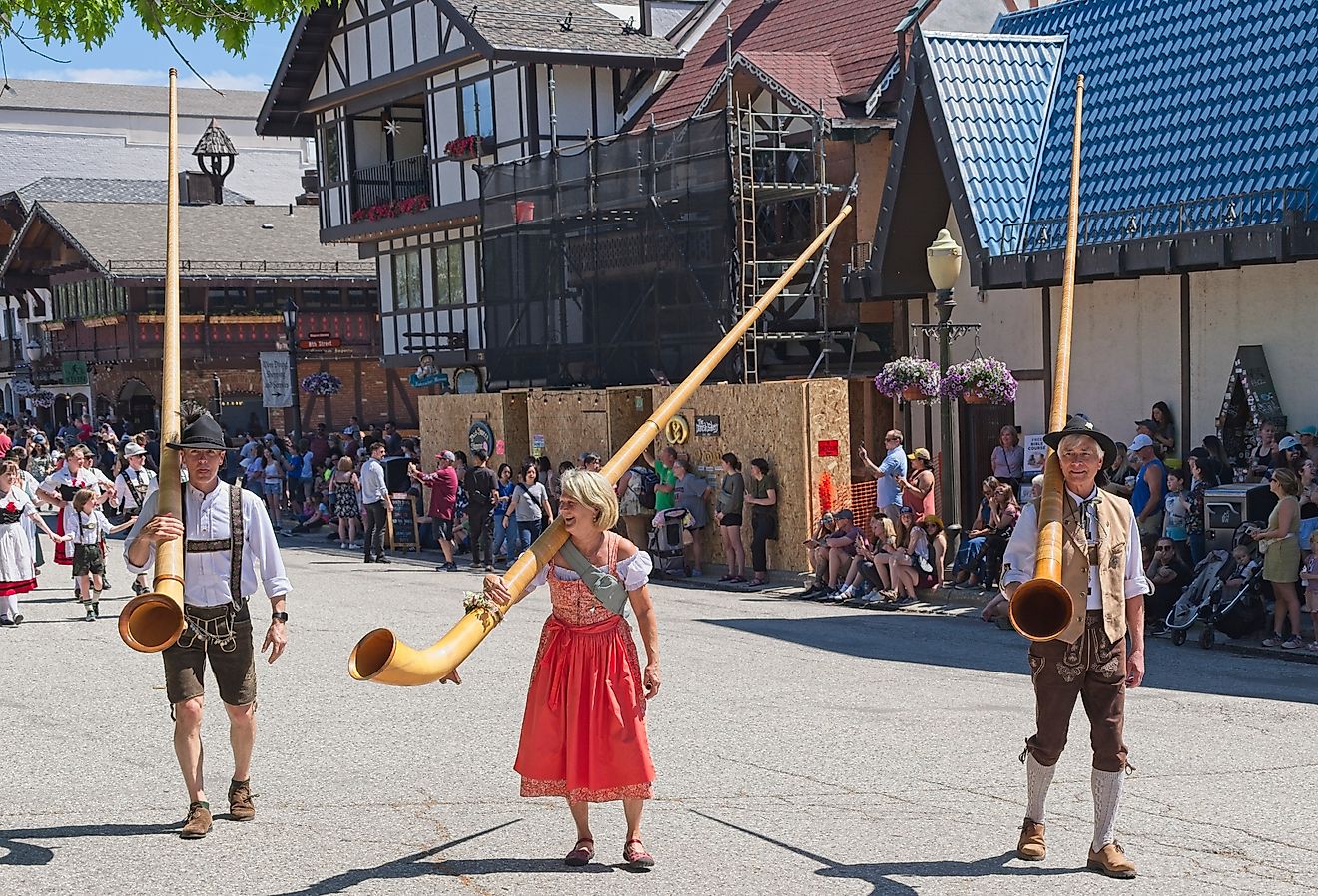 People dressed in traditional German clothes carry large alpenhorns during the Maifest celebration in Leavenworth, Washington. Image credit Gregory Johnston via Shutterstock