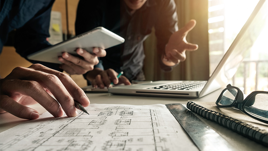 Two engineers review blueprints and working at a computer