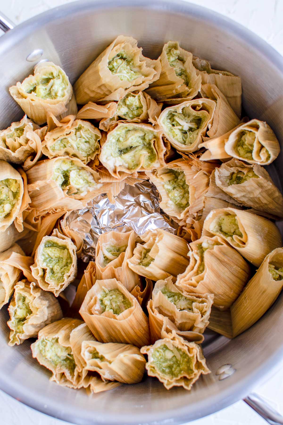 chicken tamales in corn husks standing up in a silver pot