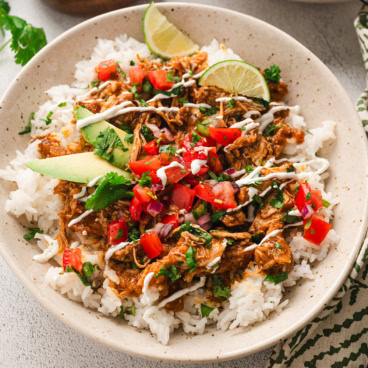 Rice bowl with shredded chicken, tomatoes, avocado and limes.