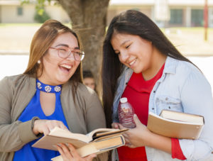 Two people laughing and smiling while holding books.