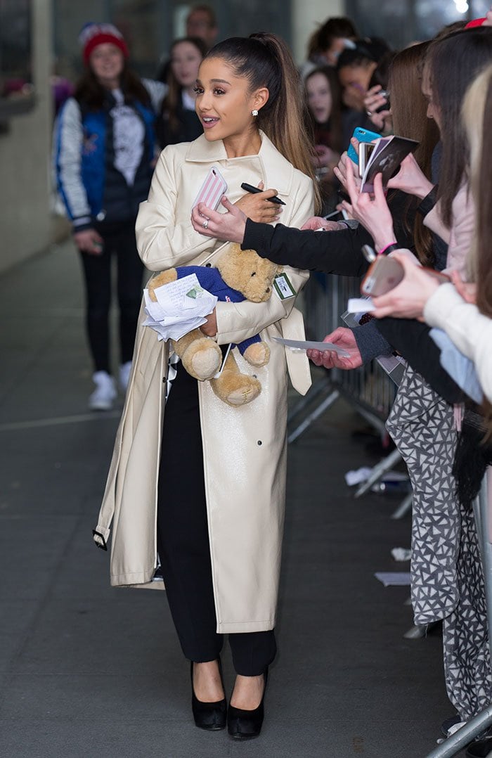 Ariana Grande holds a teddy bear and wears a trench coat while out in London