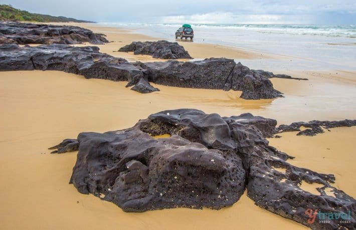 cars driving around large rocks on beach