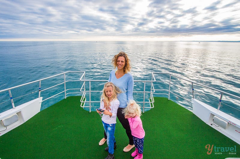 womand and kids standing on boat in the middle of ocean 