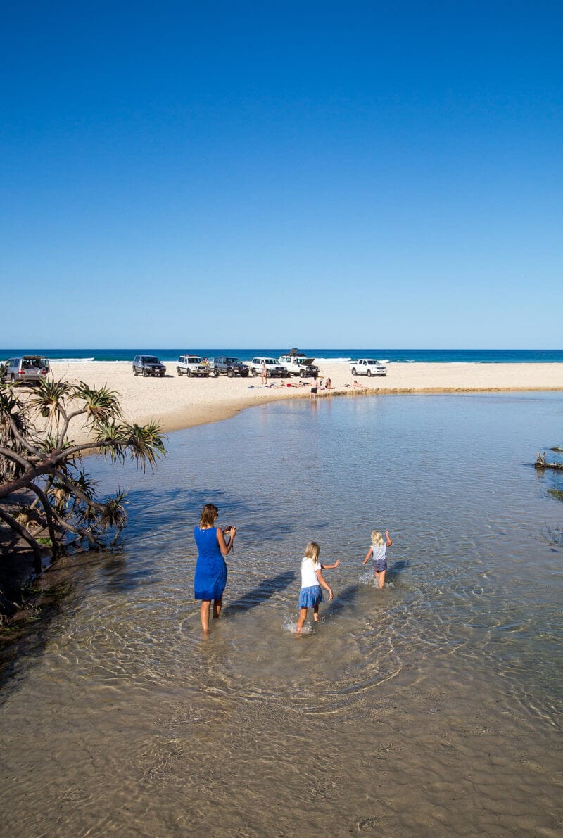 people walking along Eli Creek towards the ocean with 4WD on the beach