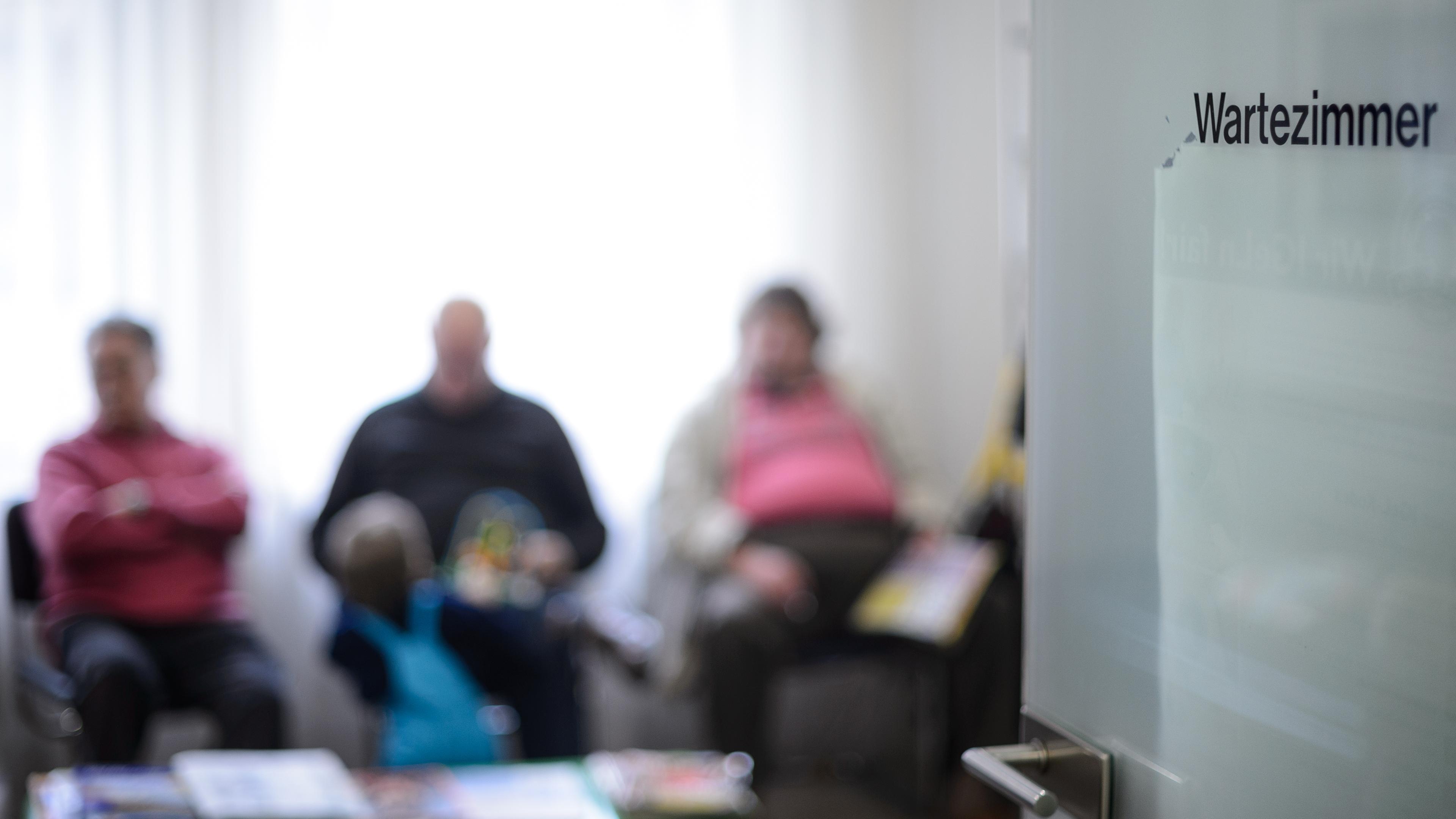 Mehrere Patienten sitzen in einem Wartezimmer, die Tür steht offen. 