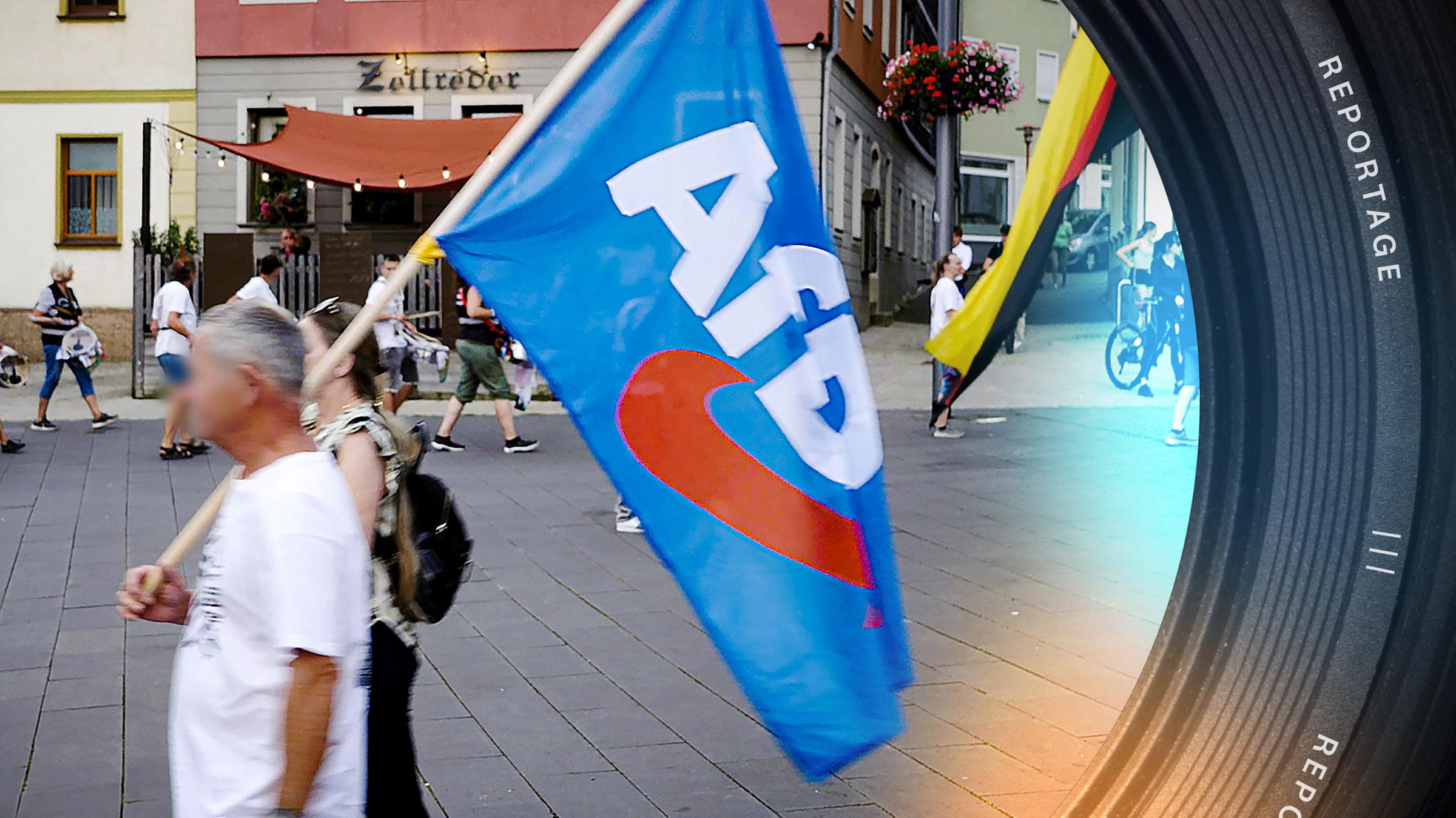 Auf dem Marktplatz in Zeulenroda laufen ein Mann und eine Frau. Er trägt eine blaue Fahne der AfD. Im Hintergrund sind weitere Demonstranten zu sehen, manche mit Trommeln und einer mit einer Deutschlandfahne.