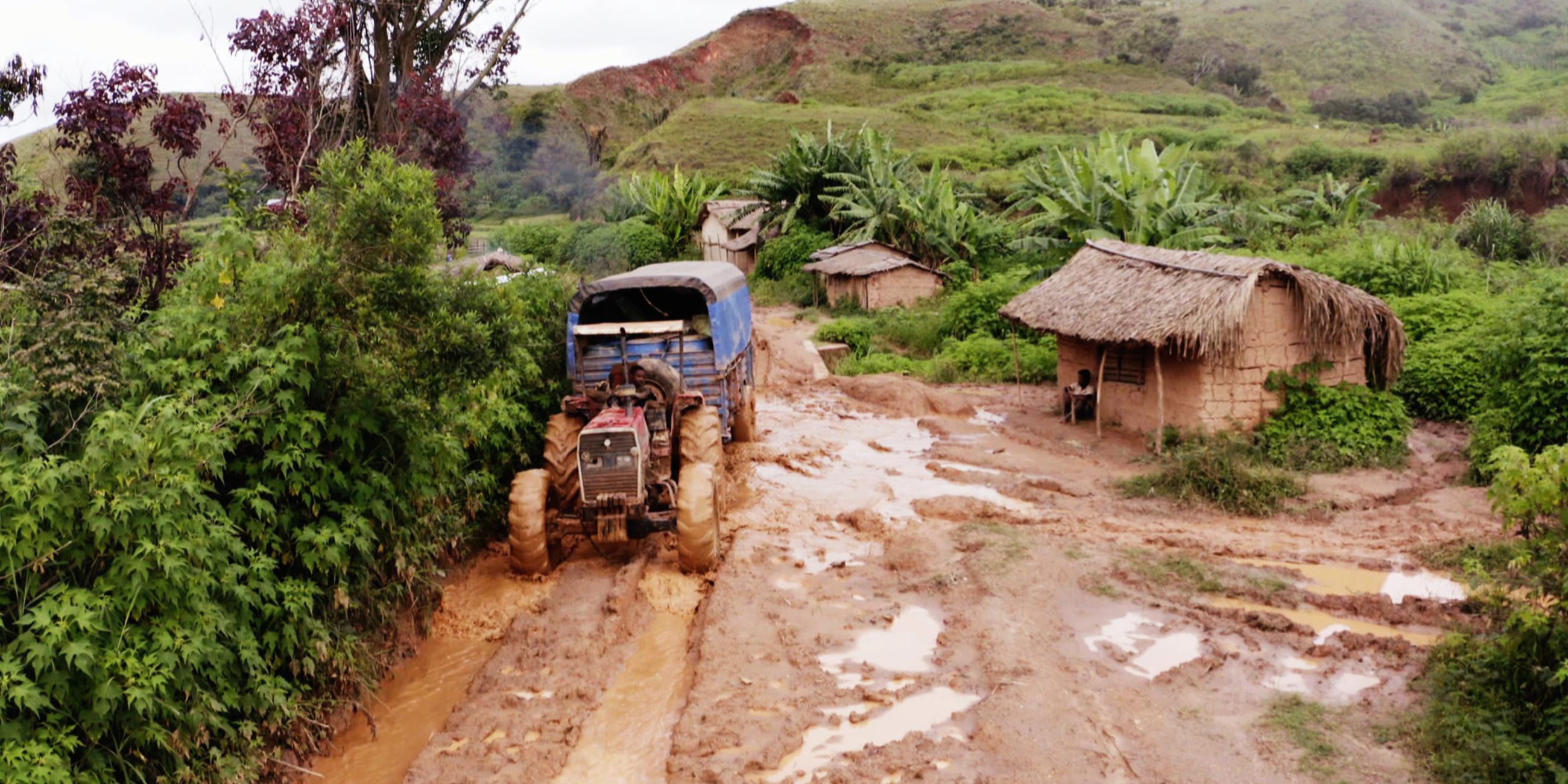 Ein Weg voller Schlamm, über den ein Traktor fährt. Daneben steht eine Hütte.