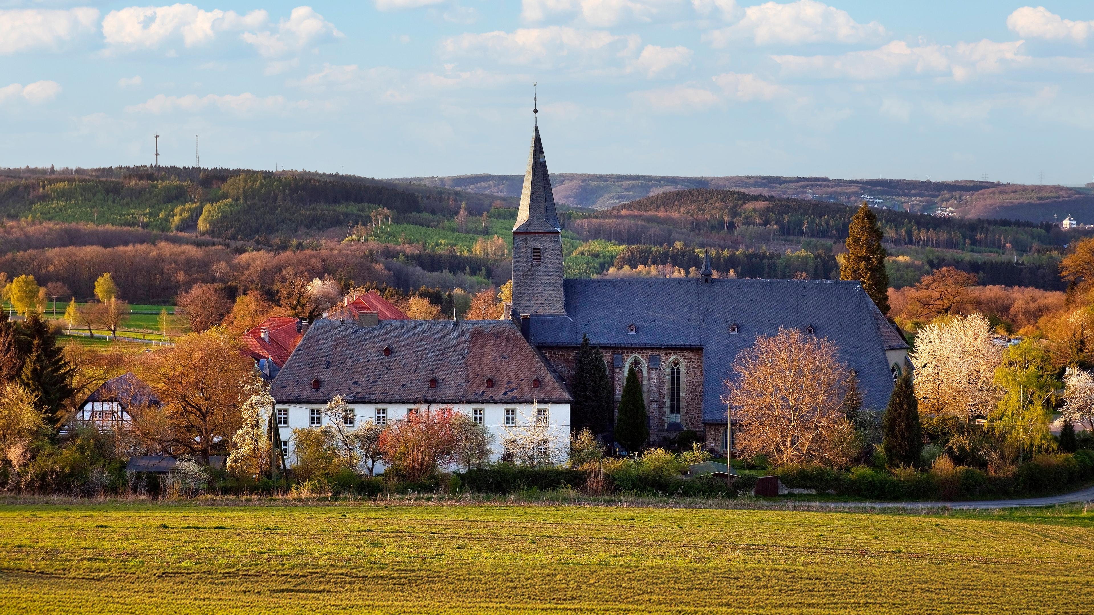 In einer herbstlichen Landschaft mit bunt gefärbtem Laub stehen alte Gebäude eng bei einer Kirche.