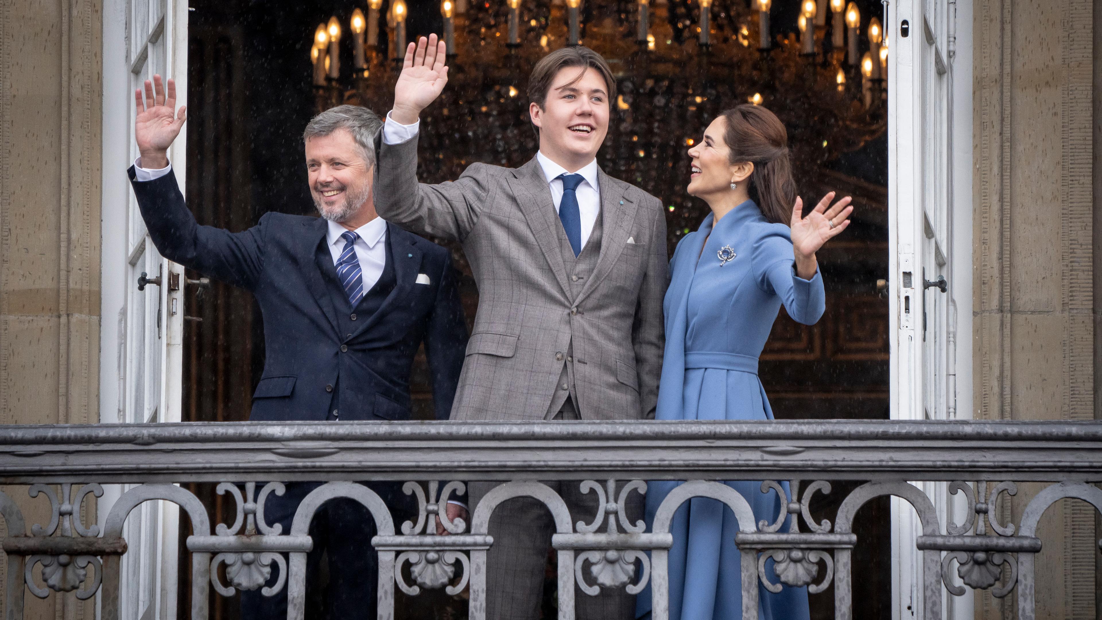 Der dänische König Frederik und seine Frau Mary stehen mit Christian in der Mitte auf dem Balkon und winken.