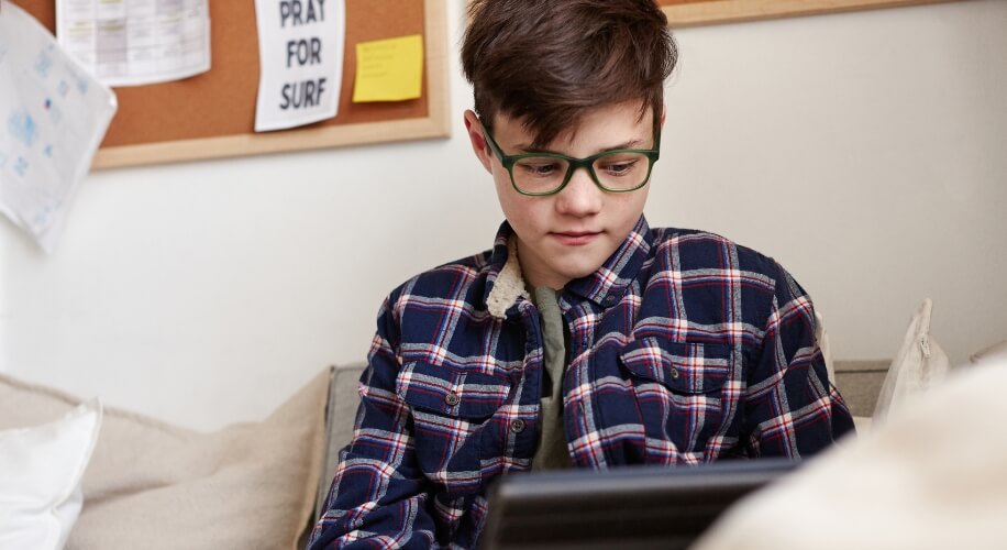 Boy wearing green glasses and a blue, red, and white plaid shirt using a tablet.