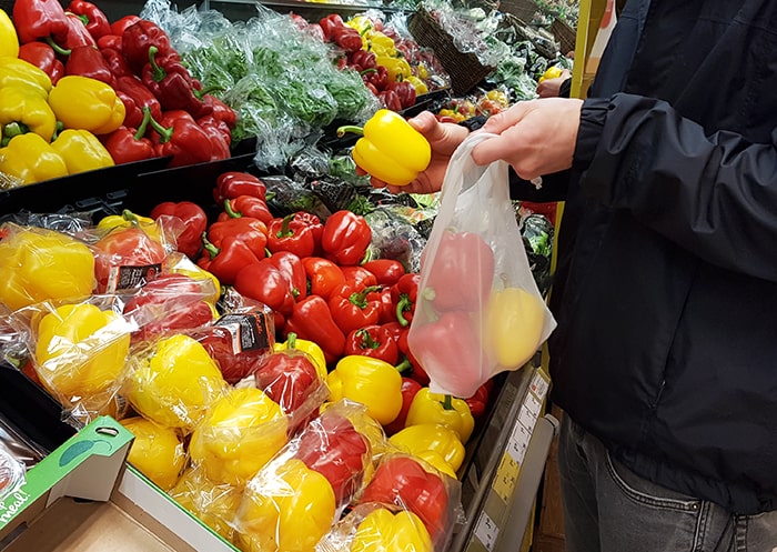 Customer in a supermarket stuffing paprika in a reusable bag.