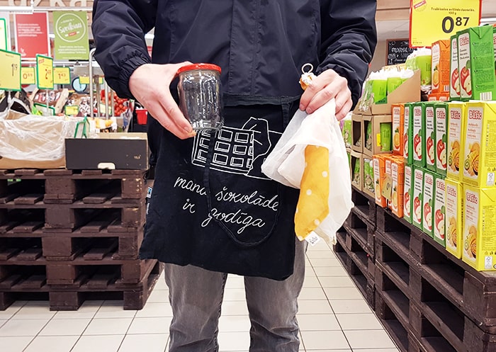 Man holding a tote bag, fabric bags, and a glass jar in a supermarket.